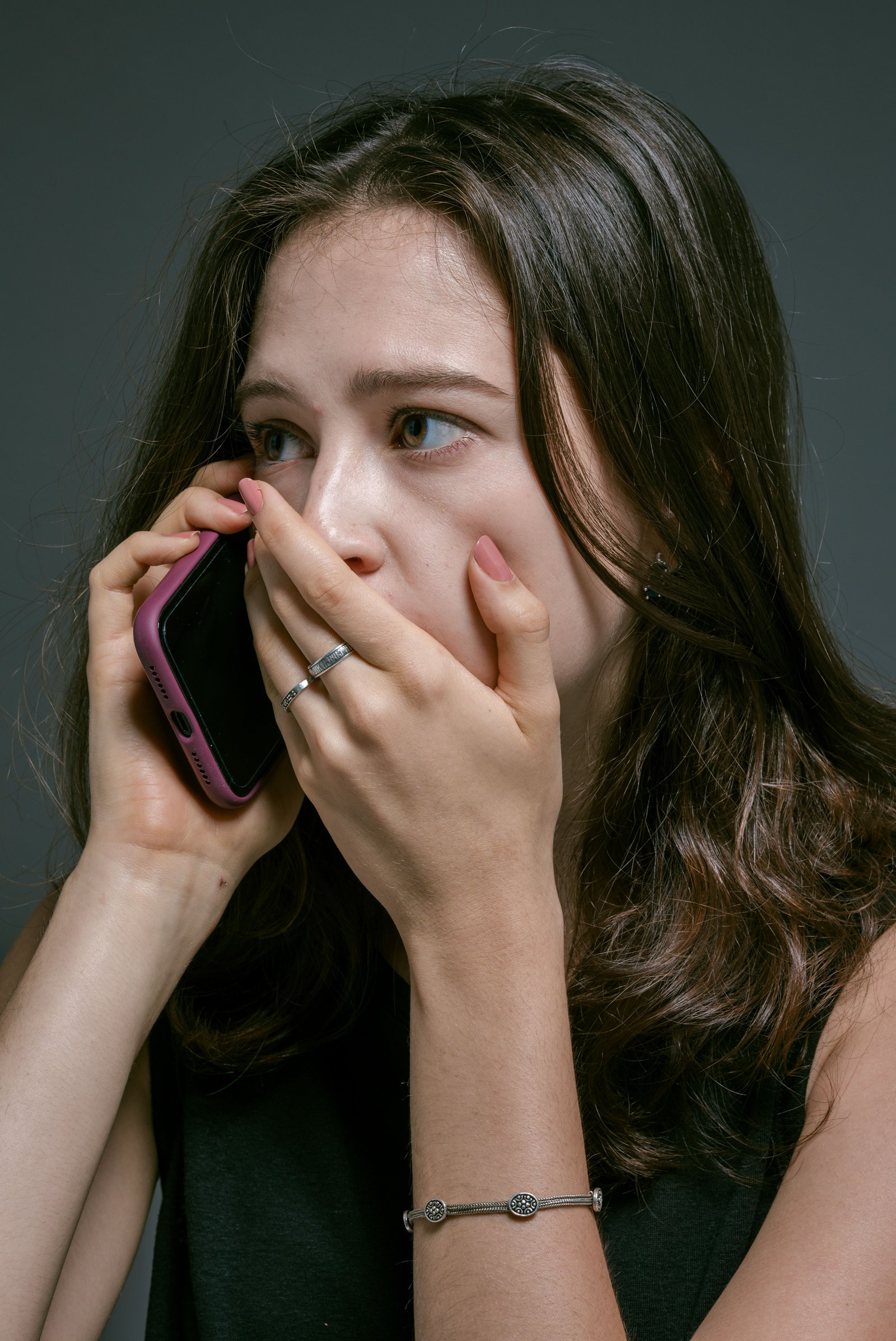 A worried young woman on the phone with her hand over her mouth